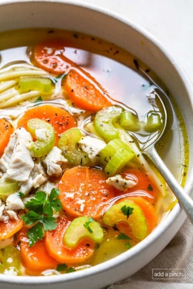 Photo of a bowl of chicken noodle soup in a white bowl with a spoon.