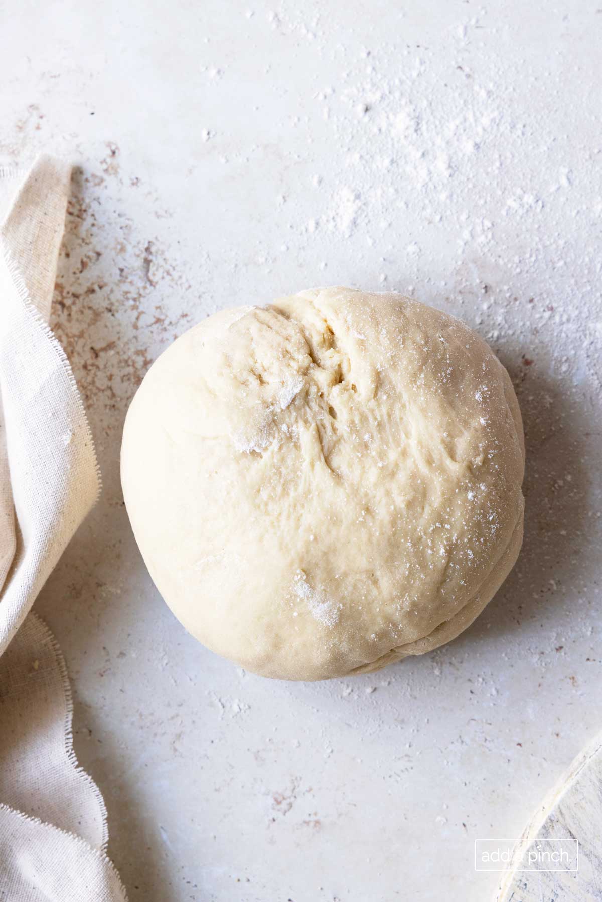 Marble counter prepped with sprinkle of flour to roll out dough holds a large dough ball with flour sprinkled on top to roll out for cinnamon rolls. 