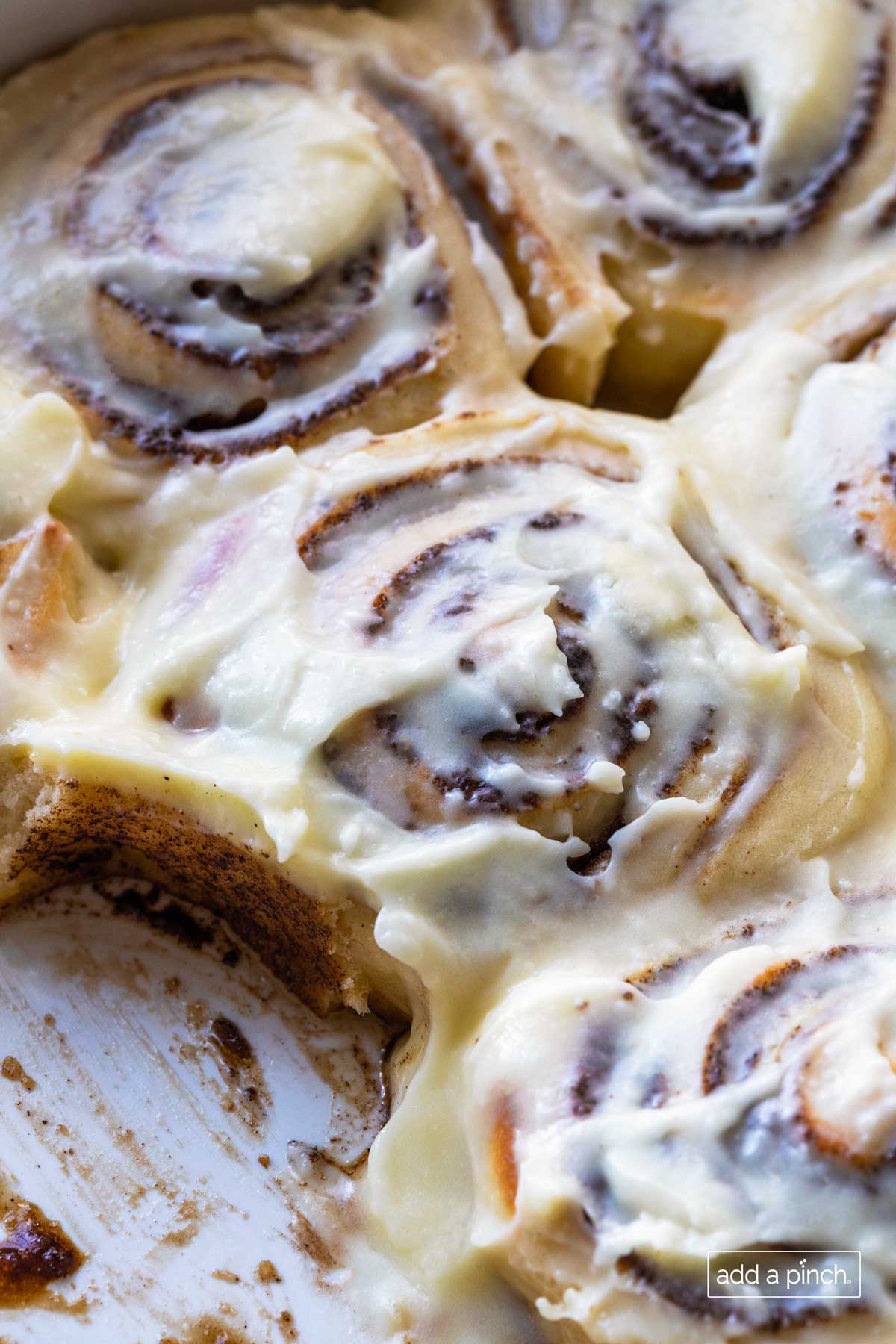 Closeup of frosted homemade cinnamon rolls with one removed from  the pan. 