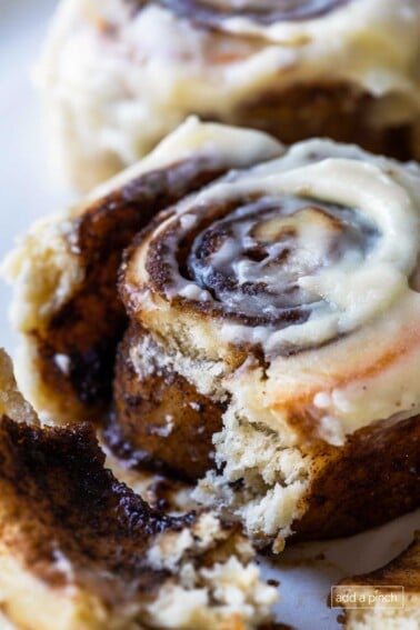 Photograph of cinnamon rolls with cream cheese frosting on a white plate with the inside with gooey cinnamon roll filling showing.