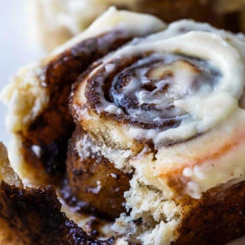 Photograph of cinnamon rolls with cream cheese frosting on a white plate with the inside with gooey cinnamon roll filling showing.