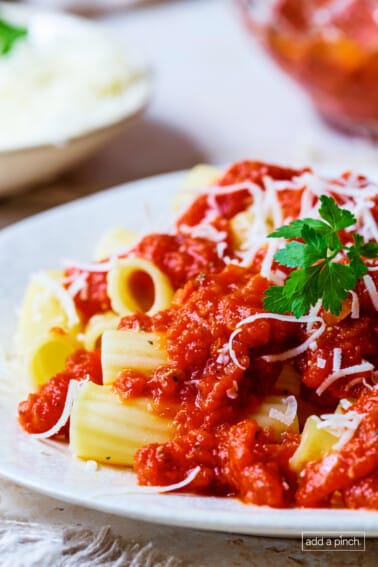 Marinara on top of cooked pasta on a white plate.