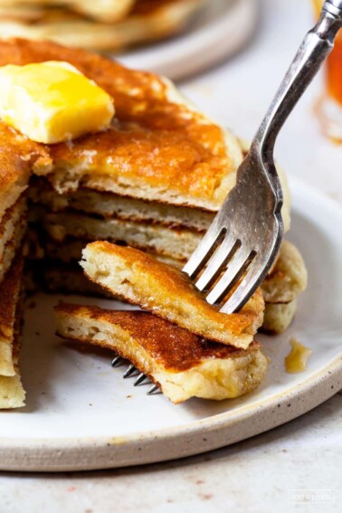 Photograph of stack of buttermilk pancakes with a bite on a fork.