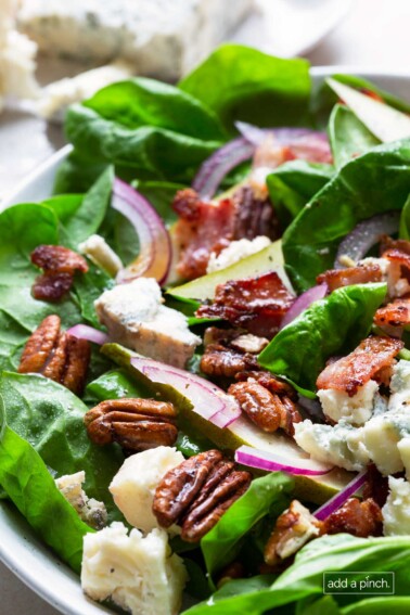 Close photograph of spinach salad with pears, bacon, onion, and blue cheese.