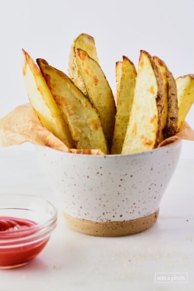 Crispy potato wedges in a pottery bowl with a ramekin of ketchup.