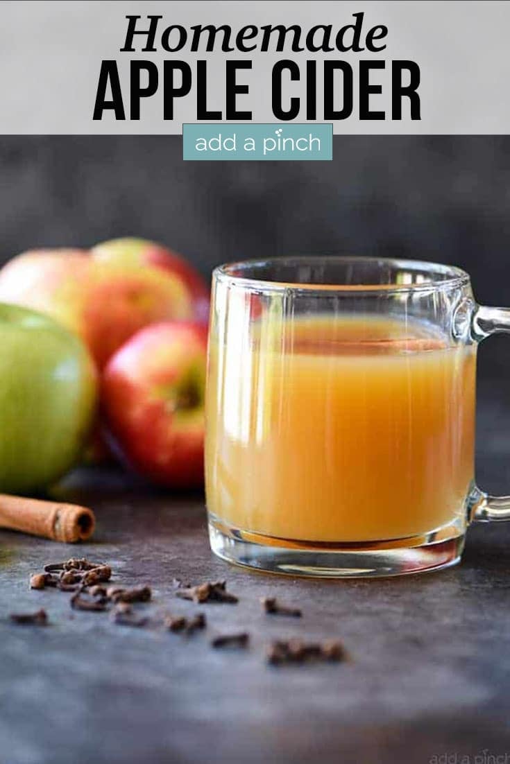 Glass mug of Homemade Apple Cider surrounded by fresh apples, cinnamon sticks and cloves - with text - addapinch.com