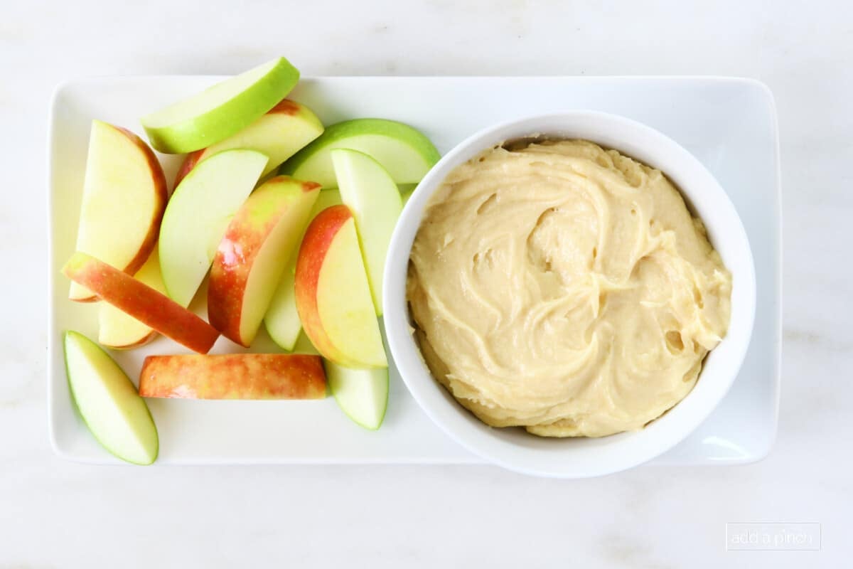 Red and green apple slices on a white platter with apple dip.