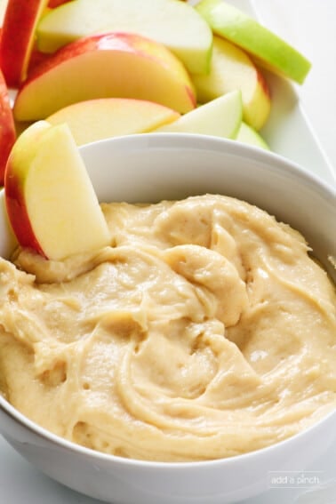 Sliced apples surround and are dipped into a bowl of creamy apple dip.