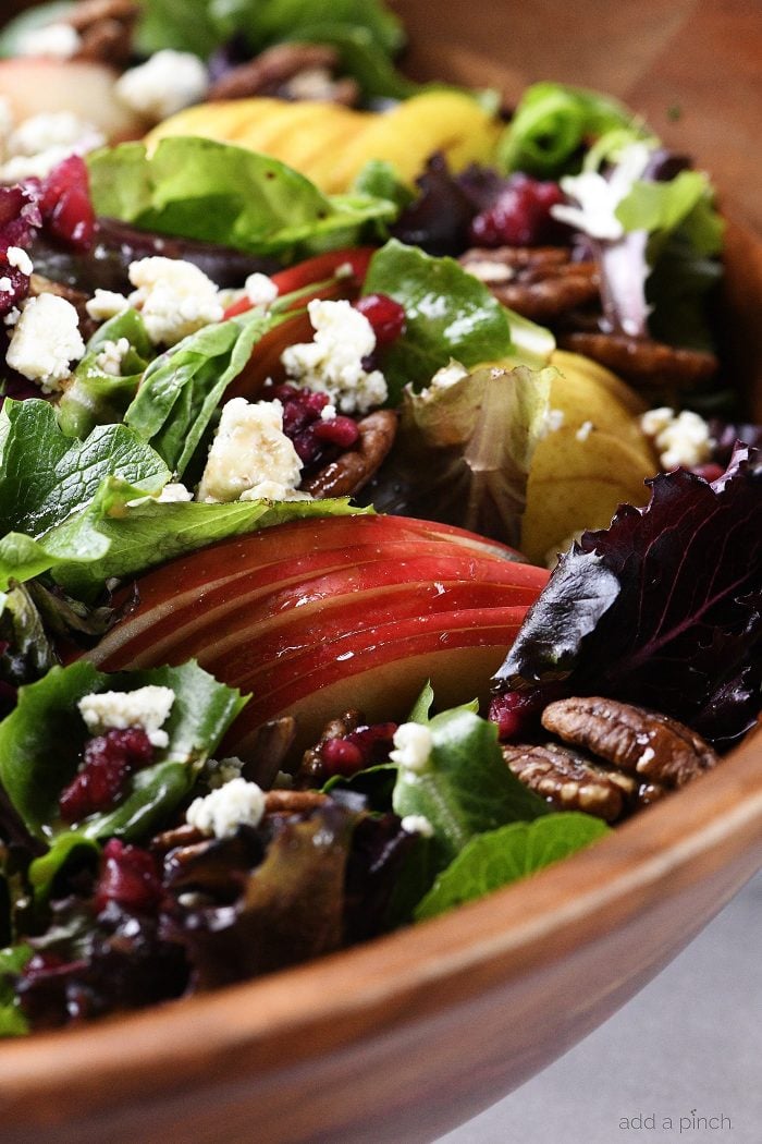 Mixed salad greens, sliced apples, sliced pears, roasted pecans, blue cheese crumbles and Pomegranate seeds in a wooden salad bowl -addapinch.com