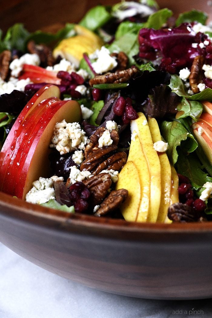 Apple Pear Salad with Pomegranate Vinaigrette and roasted pecans and blue cheese crumbles in a wooden salad bowl -addapinch.com