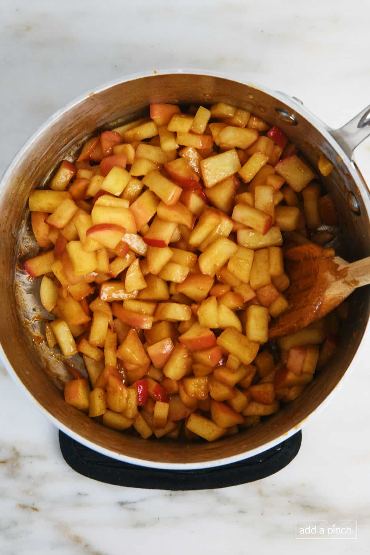 Cooked apple filling in a sauce pan with a wooden spoon.