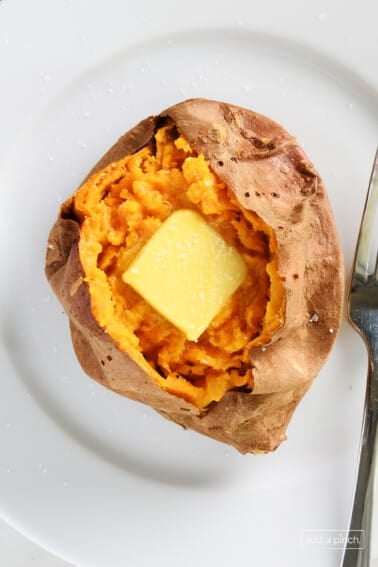 Baked sweet potato with butter and salt on a white plate with a silver fork.