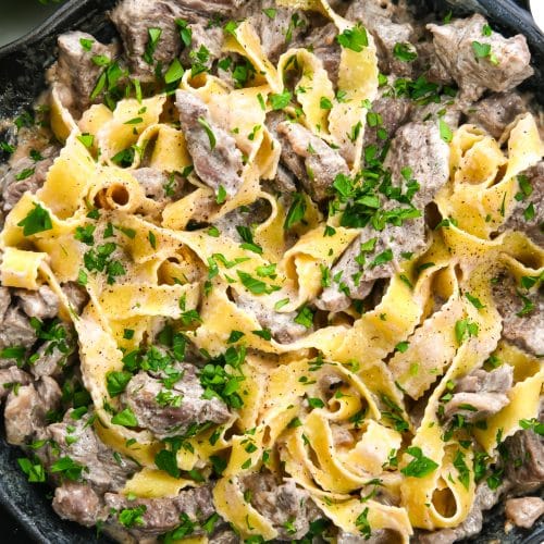 Photograph of beef stroganoff in a skillet with egg noodles and topped with parsley.