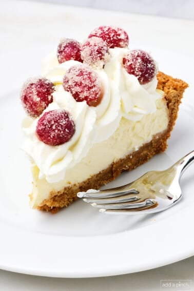 A slice of cheesecake pie topped with whipped cream and sugared cranberries on a white plate.