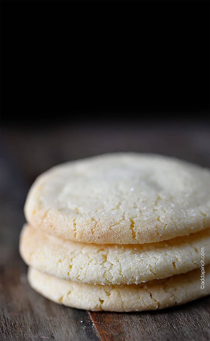 Stack of three Chewy Sugar Cookies that have been rolled in granulated sugar. On wooden board with sugar crystals on board. 