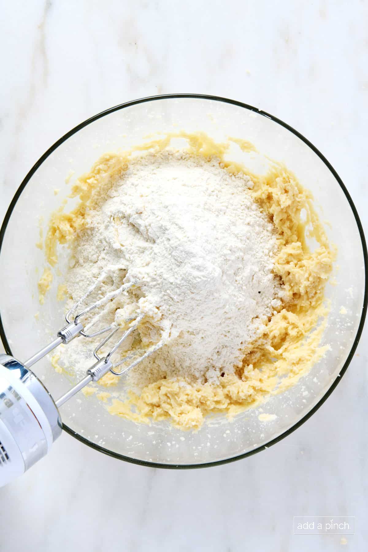 Flour added to creamed butter and sugar in a glass mixing bowl.