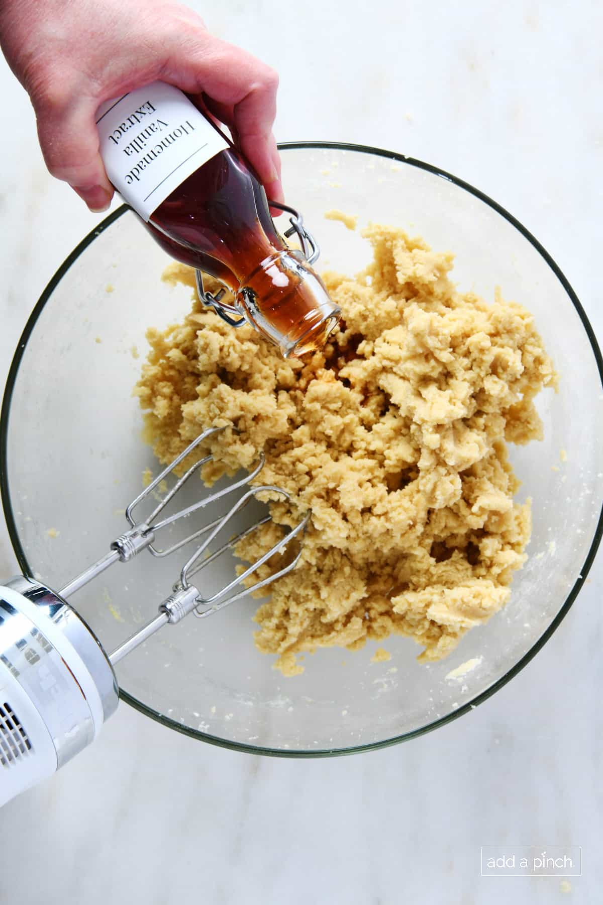 Pouring vanilla extract into sugar cookie dough in a glass mixing bowl.