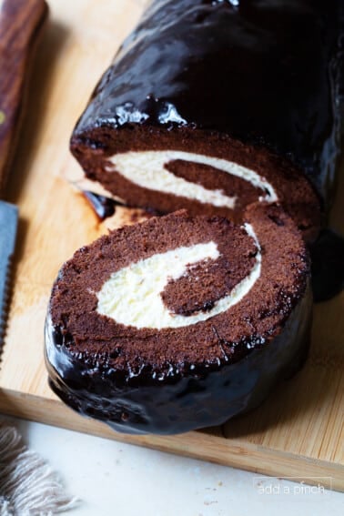 Slice of chocolate cake roll with the rest of the cake showcasing the cream filling and the roll design in the cake.