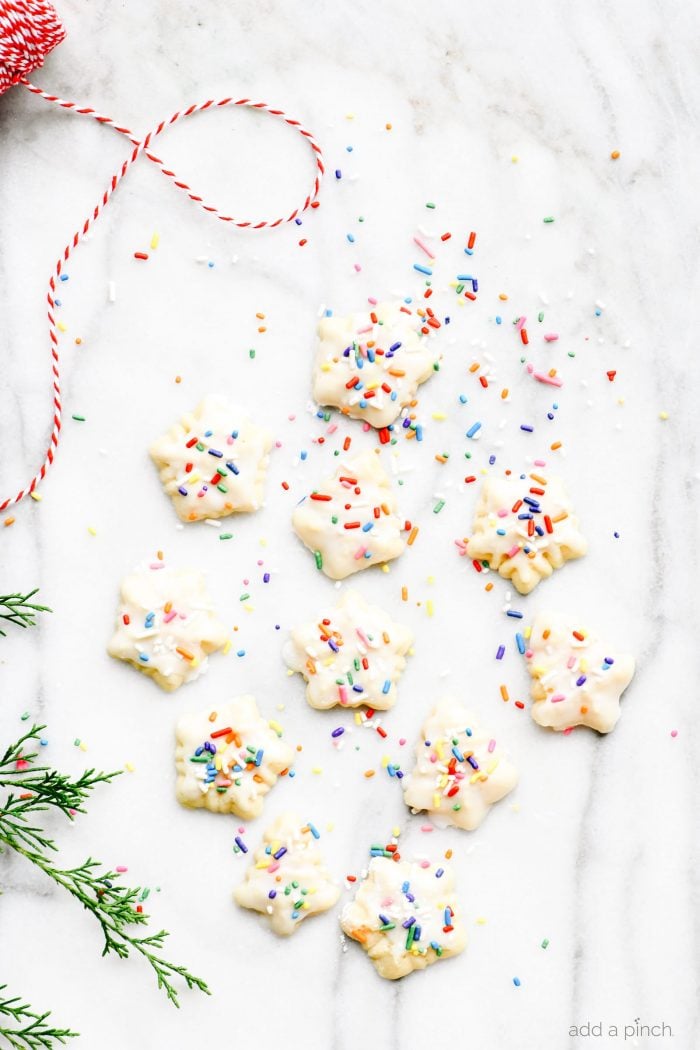 Spritz cookies glazed with multicolor sprinkles on a marble countertop surrounded by greenery and red and white twine.