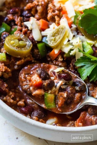 Classic chili with jalapeño, onion, grated cheese and sour cream topping. A large spoonful in a white bowl.