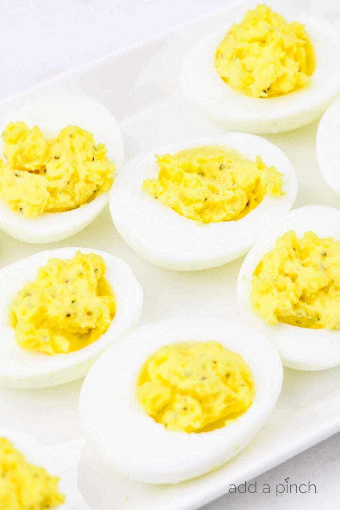 Closeup photograph of stuffed eggs on a white platter on a marble counter. 