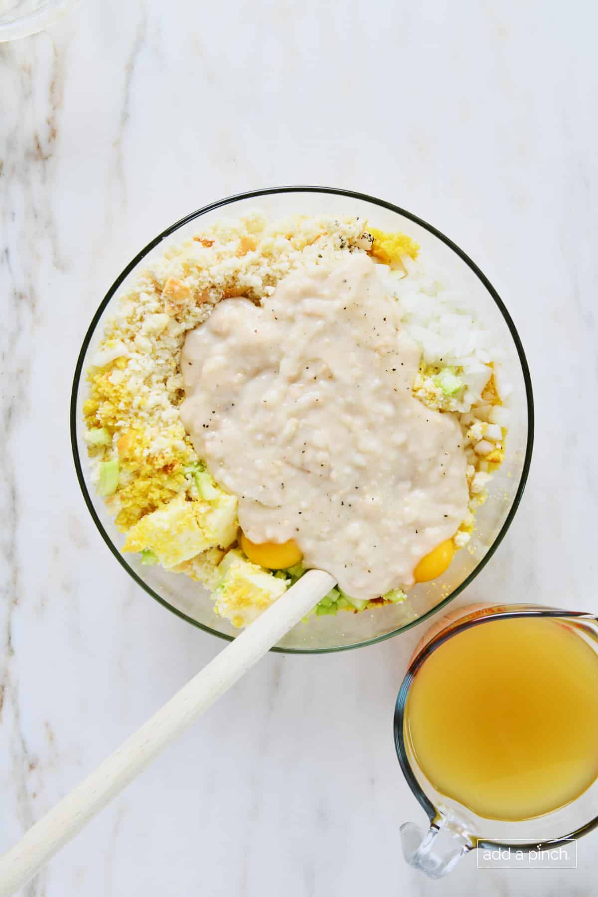 Cream of chicken soup added to cornbread dressing ingredients in a glass bowl.