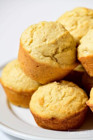 Closeup photograph of stack of cornbread muffins on a white background.