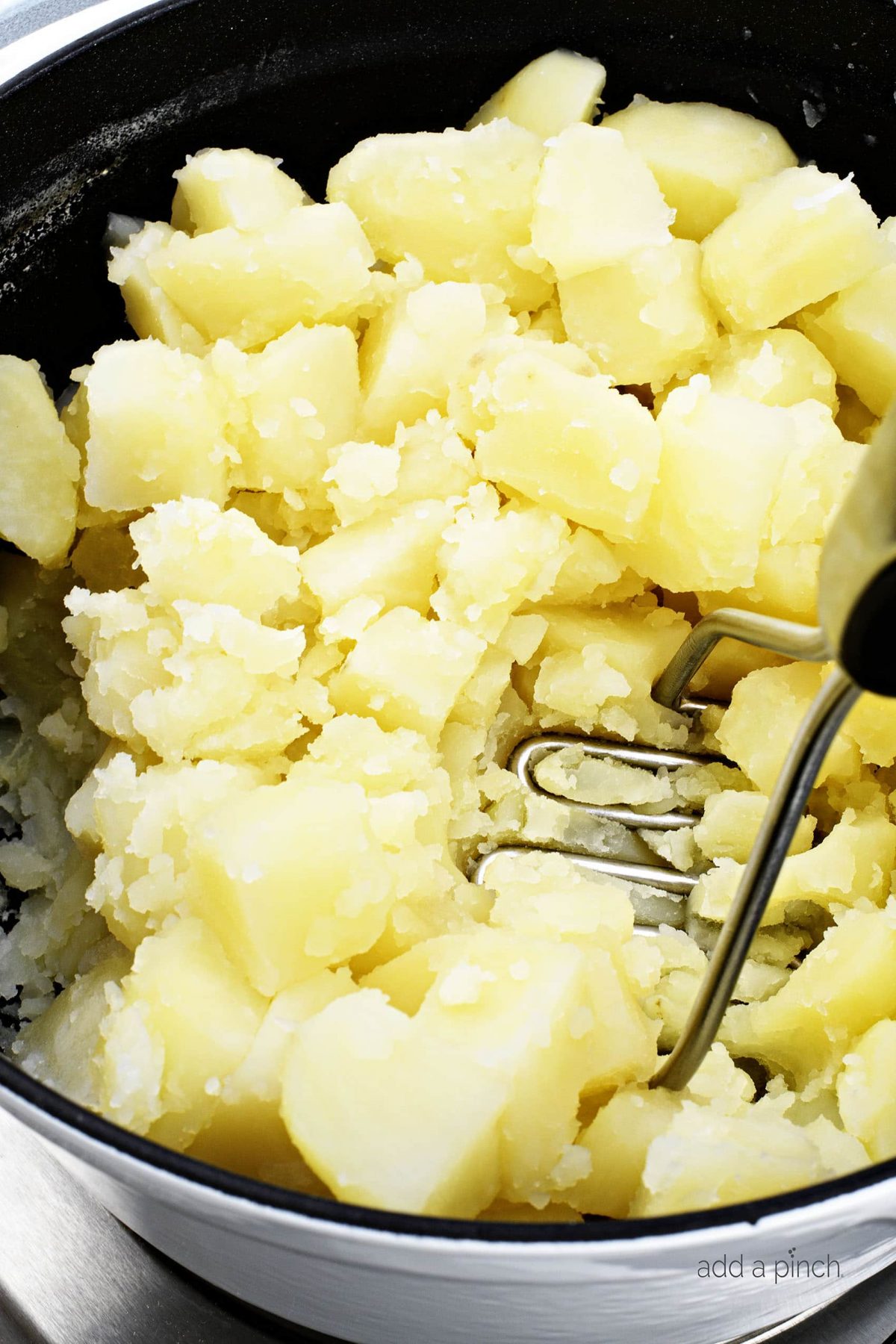 Cooked potatoes are mashed with a handheld potato masher in a large Dutch oven.