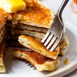 Photograph of stack of buttermilk pancakes with a bite on a fork.