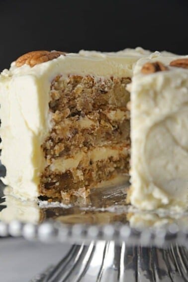 Hummingbird Cake frosted with Cream Cheese Frosting with slice removed. Served on Silver cake stand with beaded edge.