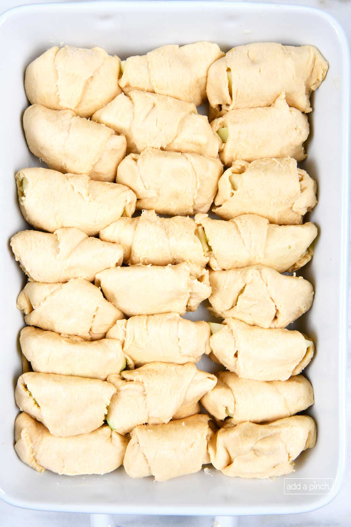 Apple dumplings in a white baking dish ready for caramel sauce.