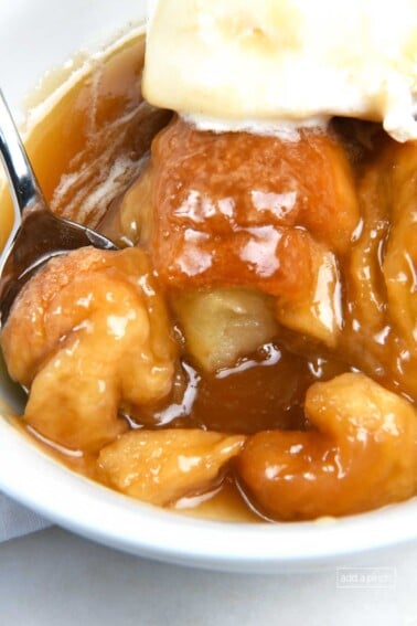 Photo of white bowl filled with baked apple dumplings topped with vanilla ice cream and caramel sauce.