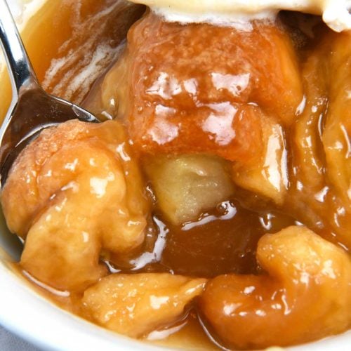 Photo of white bowl filled with baked apple dumplings topped with vanilla ice cream and caramel sauce.