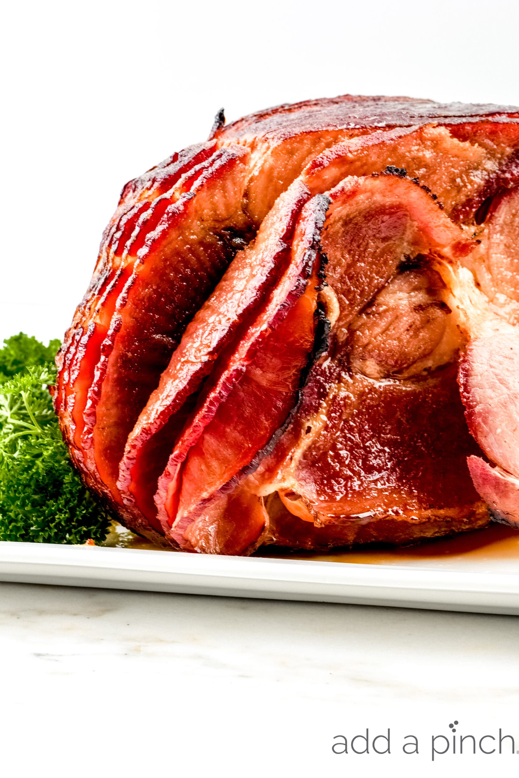 Baked Ham Recipe with fresh herb garnish on a white platter.