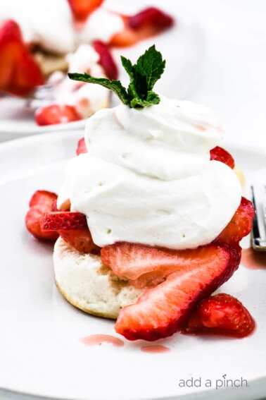 Strawberry shortcake topped with homemade whipped cream and mint sprig on a white plate. // addapinch.com