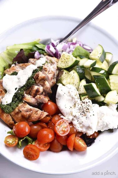  Grilled Chicken Salad with Pesto Ranch Dressing Recipe makes a delicious salad with cucumbers, tomatoes, onion, mozzarella topped with grilled chicken and a pesto ranch dressing! // addapinch.com