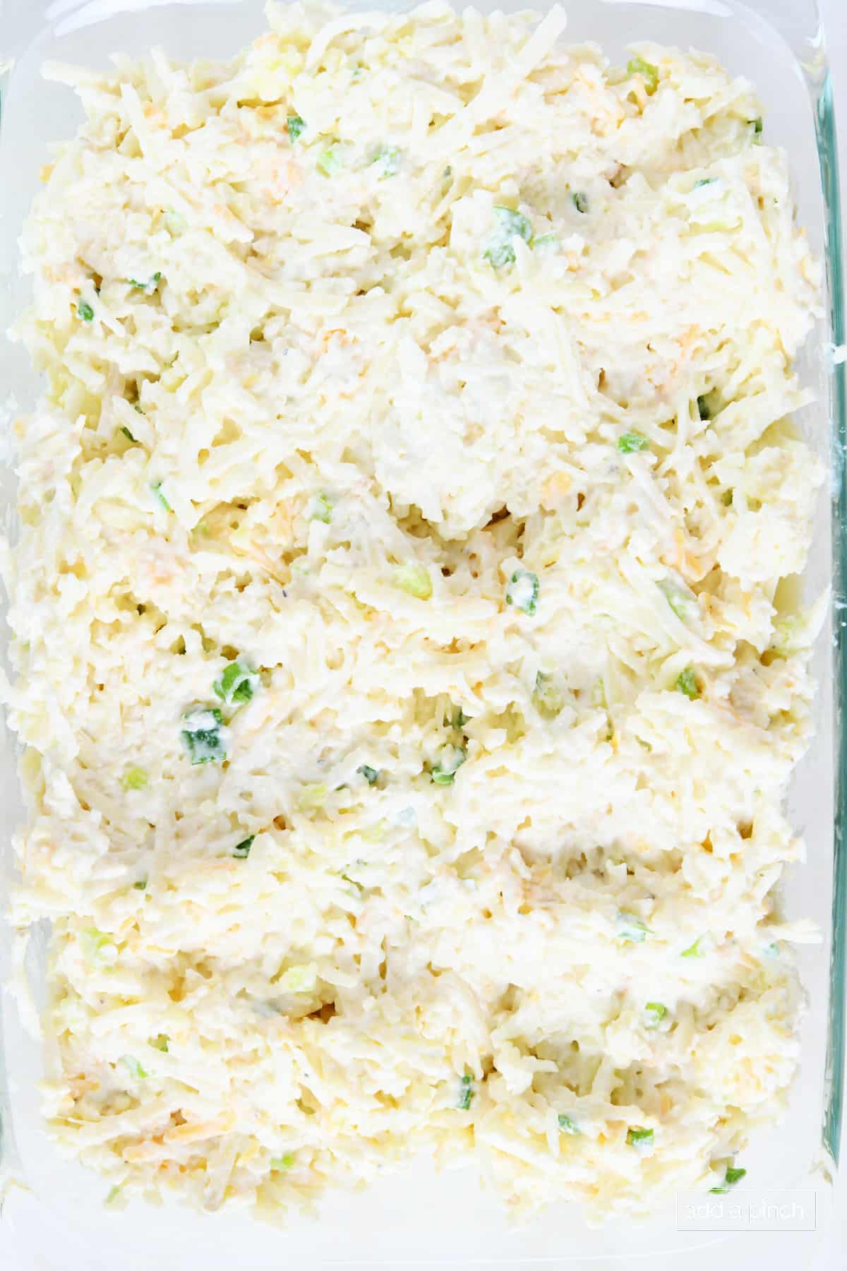 Glass baking dish holds uncooked hashbrown casserole before the cheese is added.