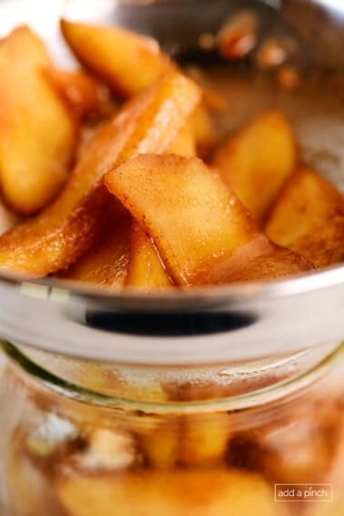 Apple pie filling is decanted into a glass jar.