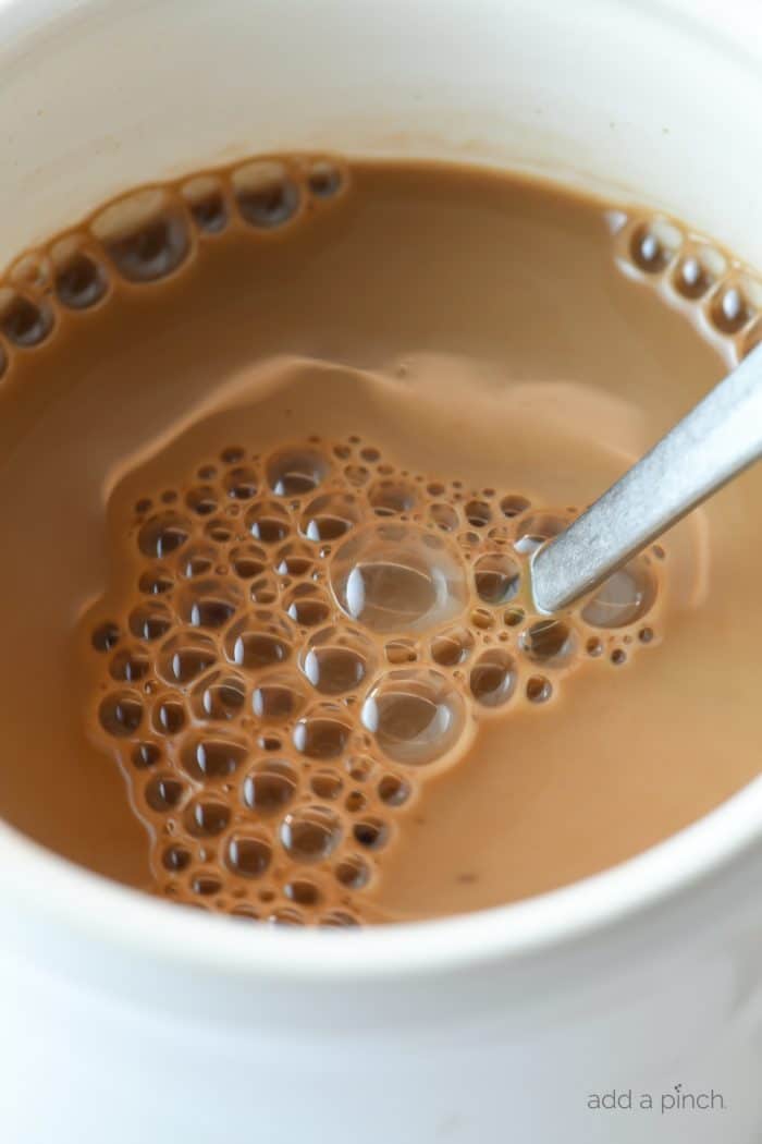 Closeup photograph of hot cocoa in a white mug with a spoon. // addapinch.com