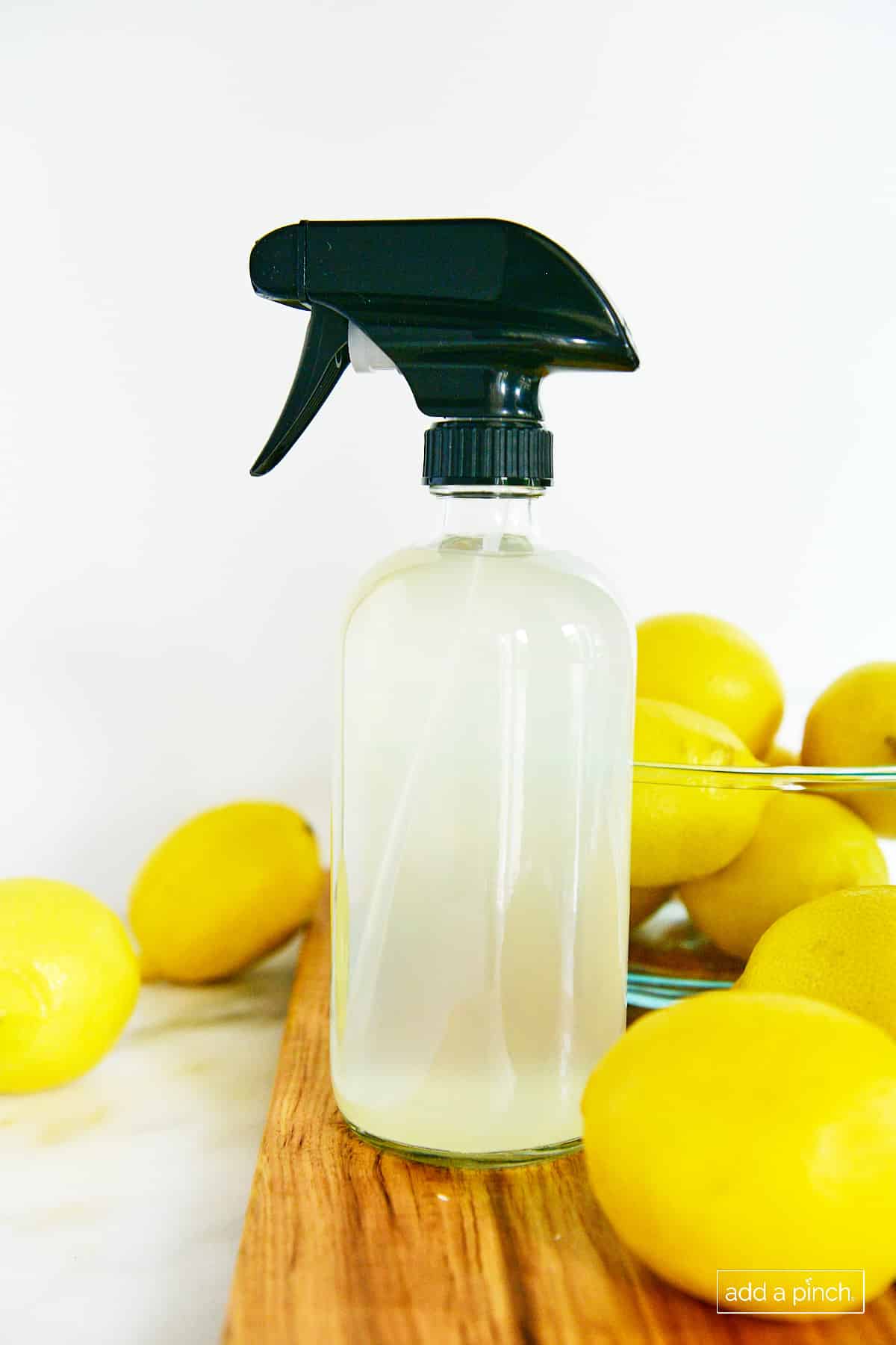 photo of glass spray bottle containing a cloudy liquid on a cherry. board with yellow lemons on a marble surface