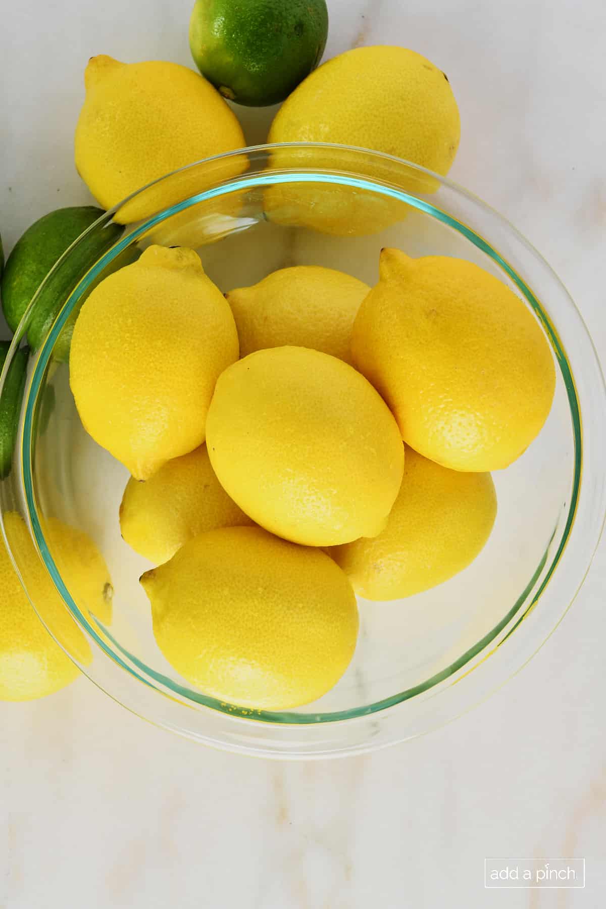 photo of clear bowl with yellow lemons with yellow lemons and green limes on a marble surface