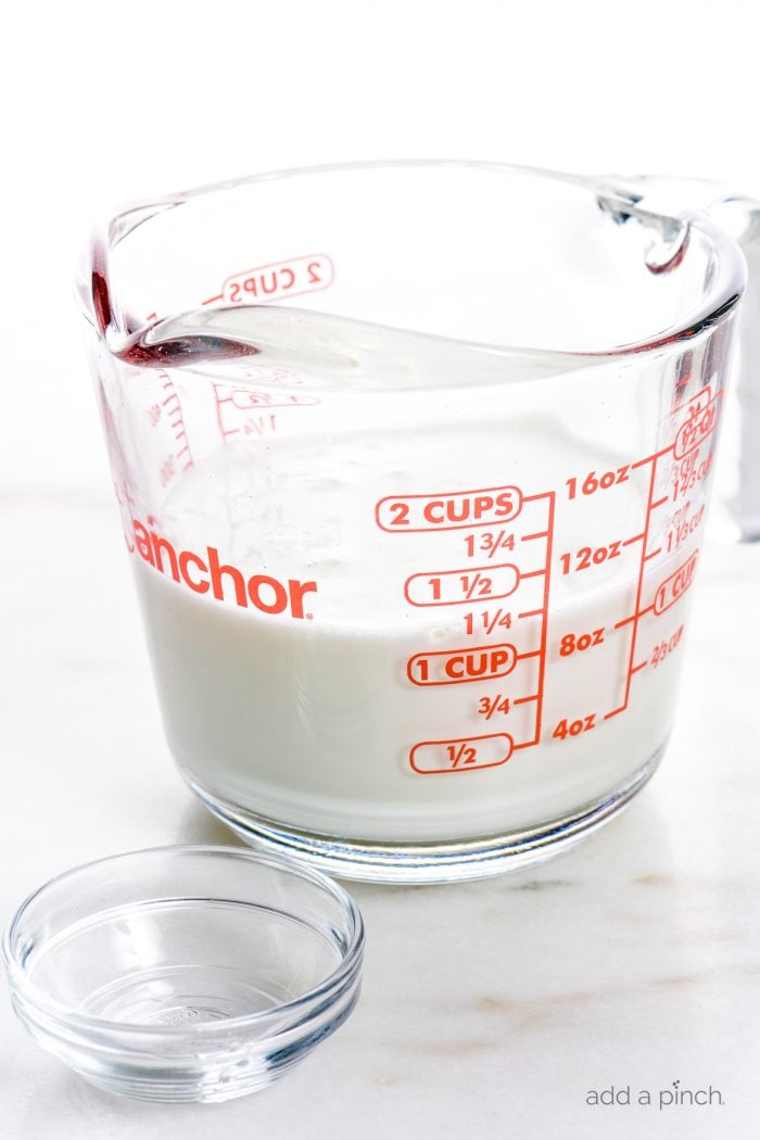 Glass measuring cup with milk and glass bowl with vinegar to make buttermilk substitute.