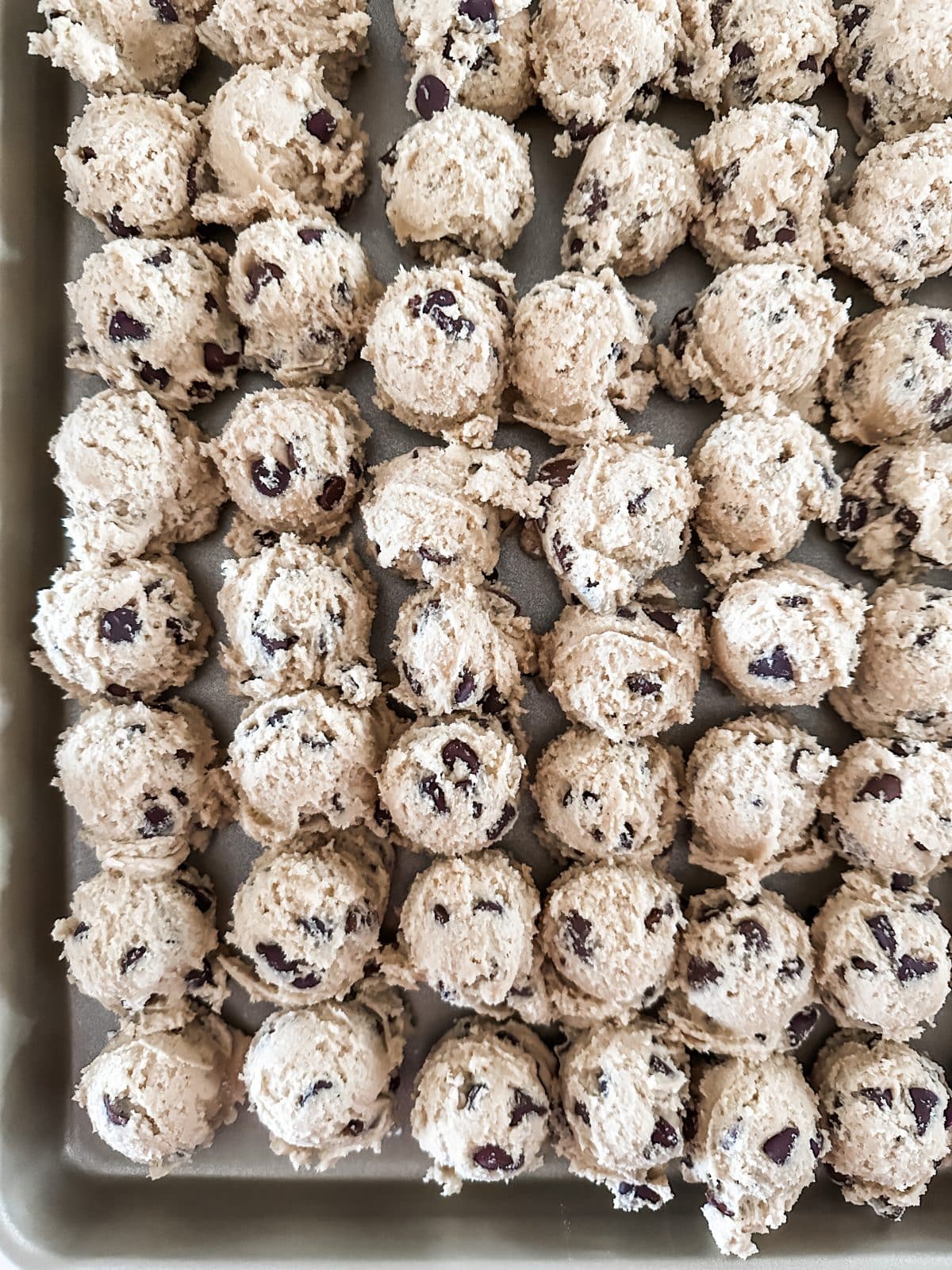 Photo of scoops of frozen chocolate chip cookie dough on a baking sheet.