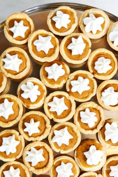 Mini pumpkin pie topped with whipped cream on a pewter plate.