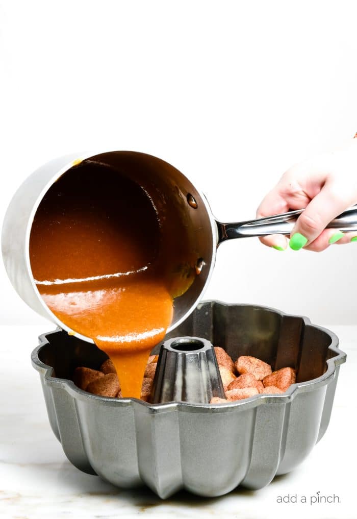 Photograph of caramel pouring over unbaked monkey bread in a bundt pan ready to go in the oven for baking. 