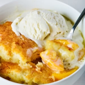 Photo of peach cobbler in a white bowl with vanilla ice cream