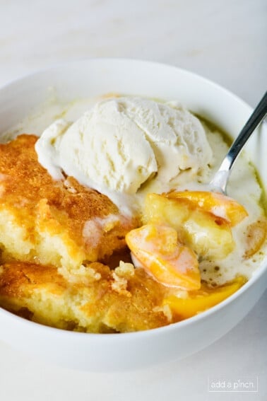 Photo of peach cobbler in a white bowl with vanilla ice cream