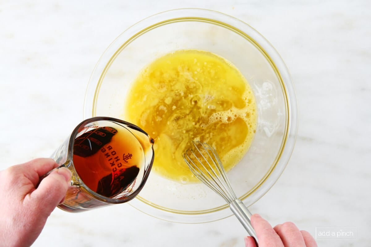 Adding maple syrup to sugar and egg mixture in a glass bowl.