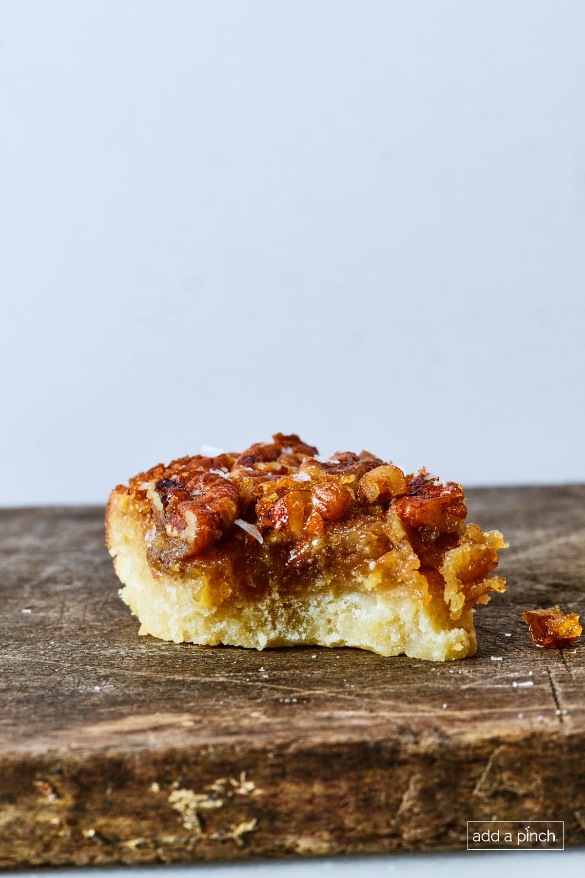 Pecan pie bar on a wooden board with a bite out of it.