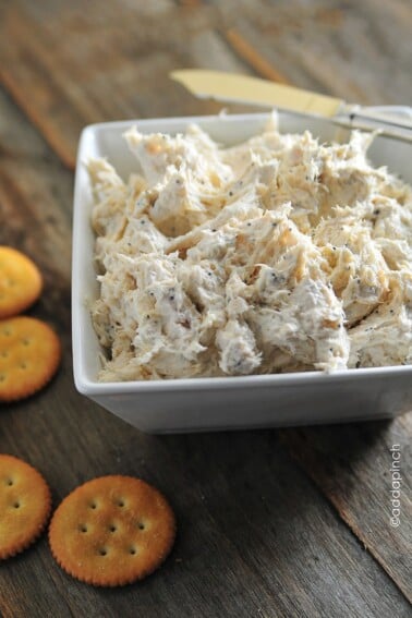 Image of poppy seed chicken dip in a white bowl with crackers around the bowl. All placed on a wooden surface.